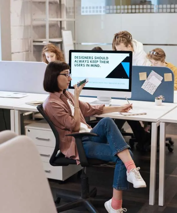 Digital marketers working in a bright, modern office, focused on their laptops and desktops. The team is seated at desks, collaborating and analyzing data on screens.