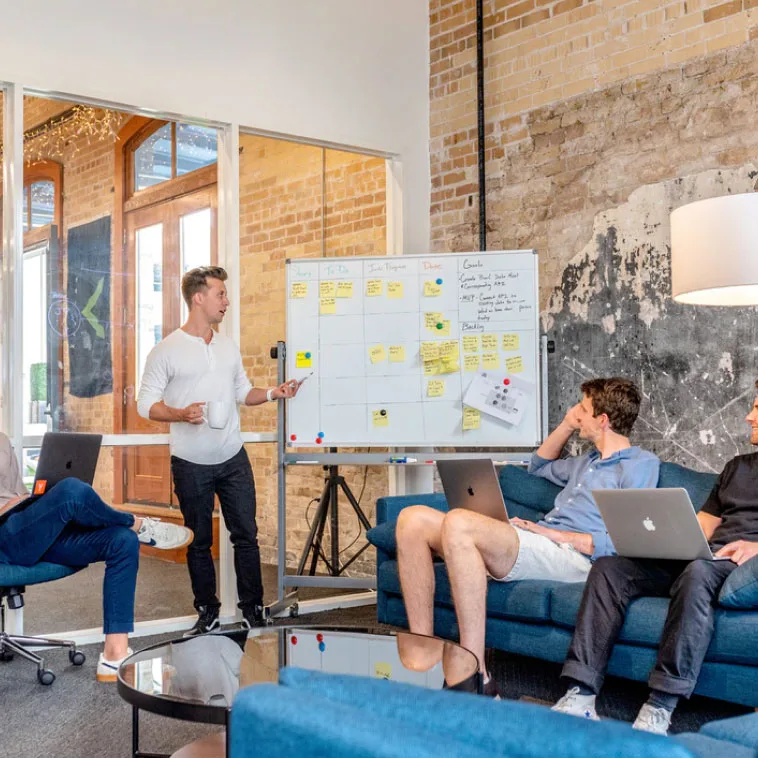 Digital marketers discussing strategy, gathered around a whiteboard covered with diagrams and notes, actively brainstorming ideas.